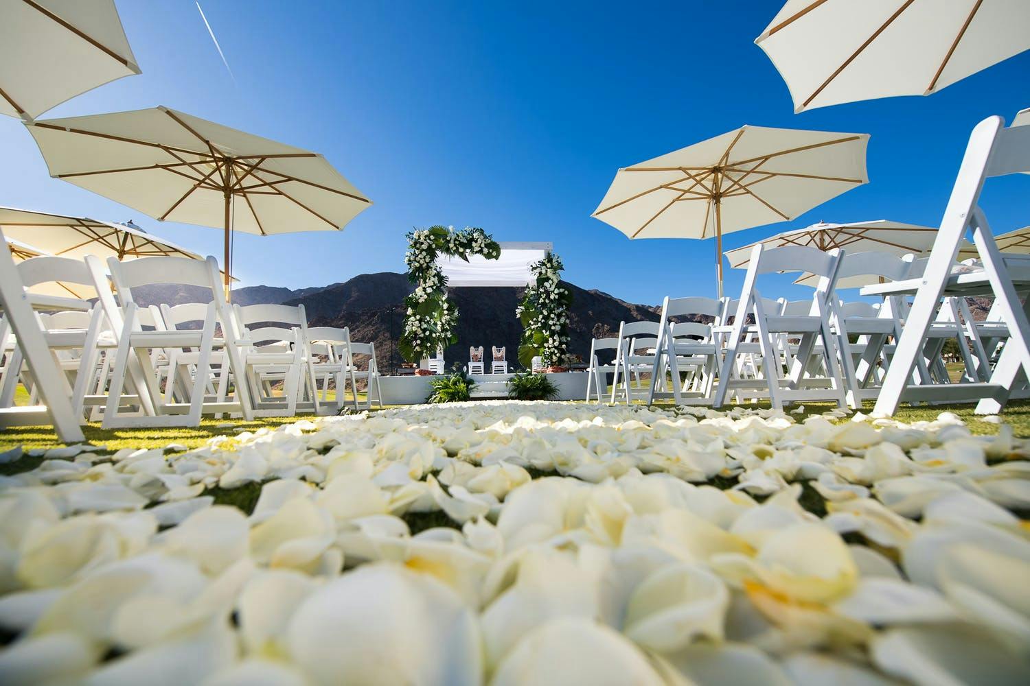 Desert wedding with white petals on aisle lined with white shady umbrellas | PartySlate