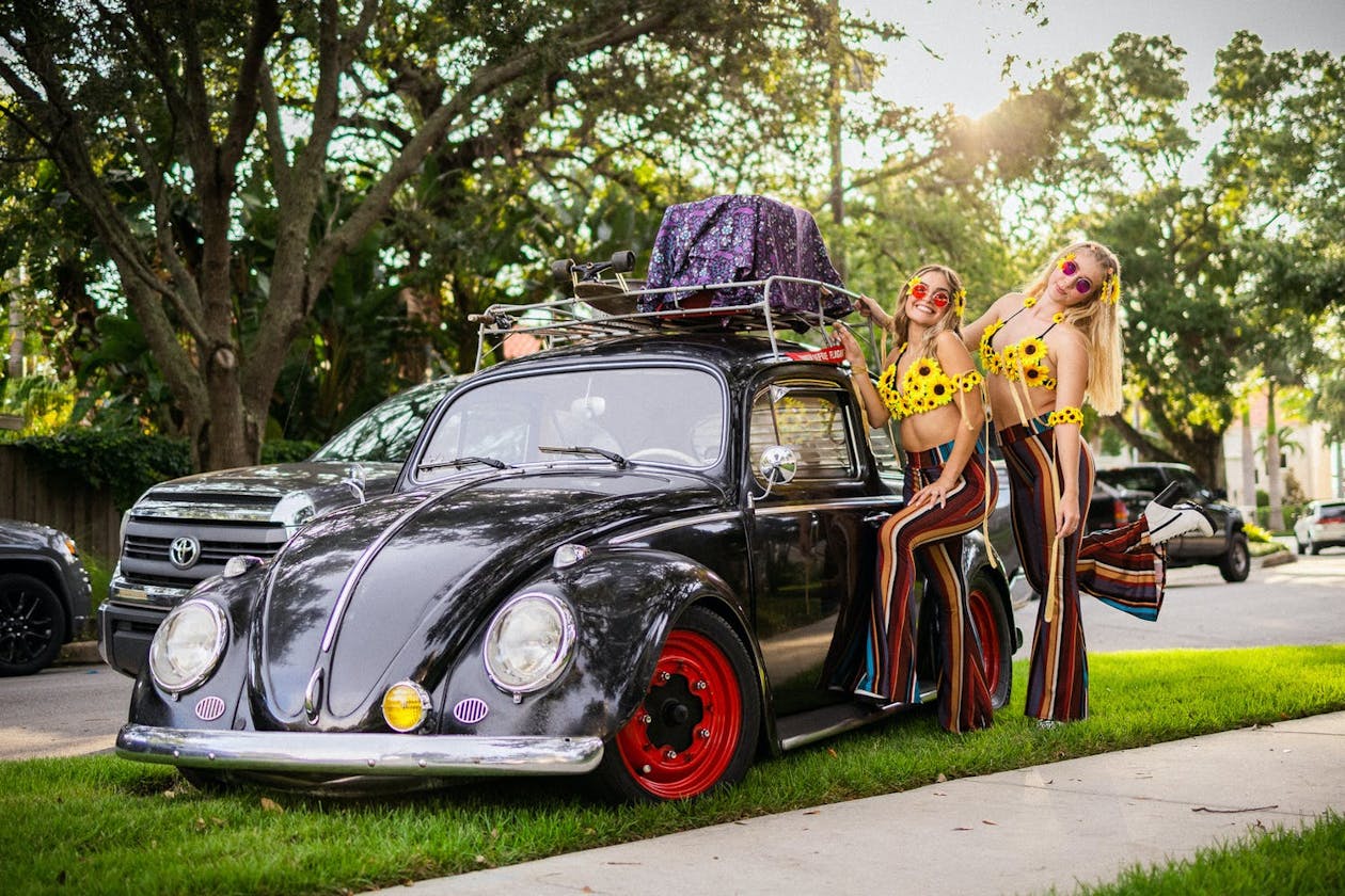 Woodstock Inspired Party With Neon Lights and Two Girls Dressed in Sunflower Outfits Standing by Vintage Volkswagon Beetle | PartySlate