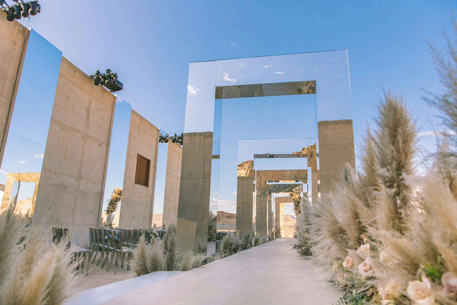 Wedding aisle lined with mirrored archways and pampas grass in desert landscape | PartySlate