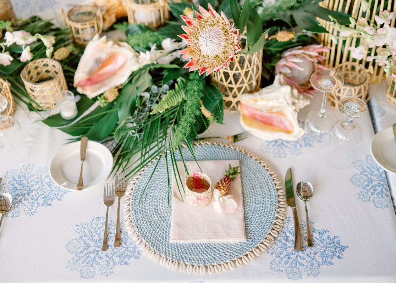 Tropical centerpieces with protea flowers in wicker vases | PartySlate