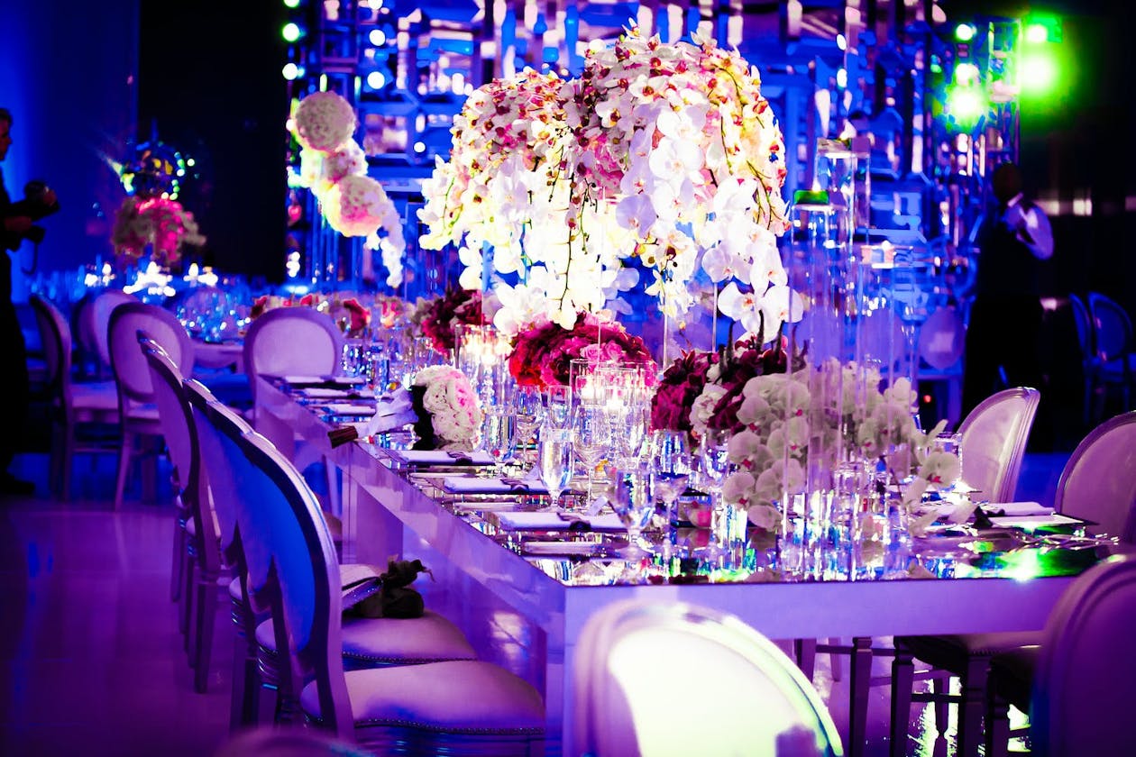 Modern ballroom wedding with white orchid centerpieces with hot pink accents, mirrored tabletops, and blue and purple uplighting | PartySlate