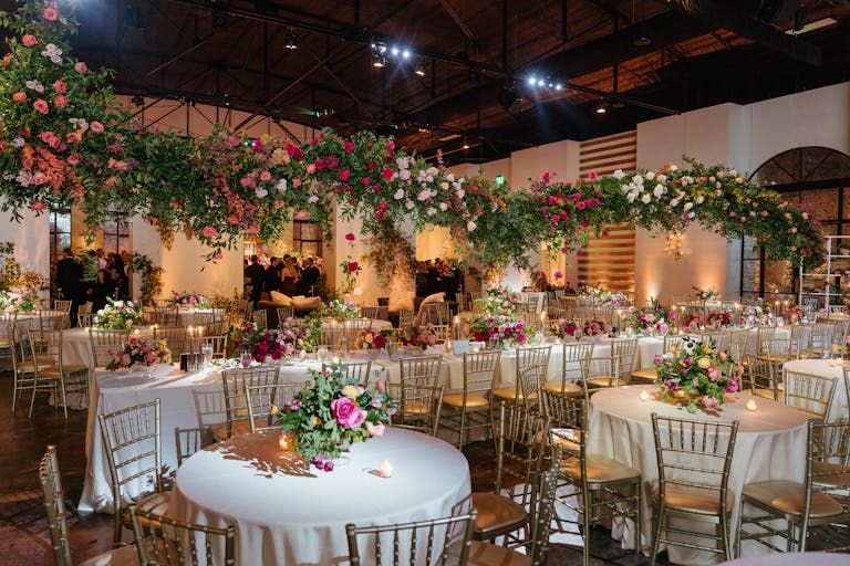 Wedding Venue in Houston Texas With Tables in Chairs Covered in Linen and Floral Installation Hanging From Ceiling | PartySlate
