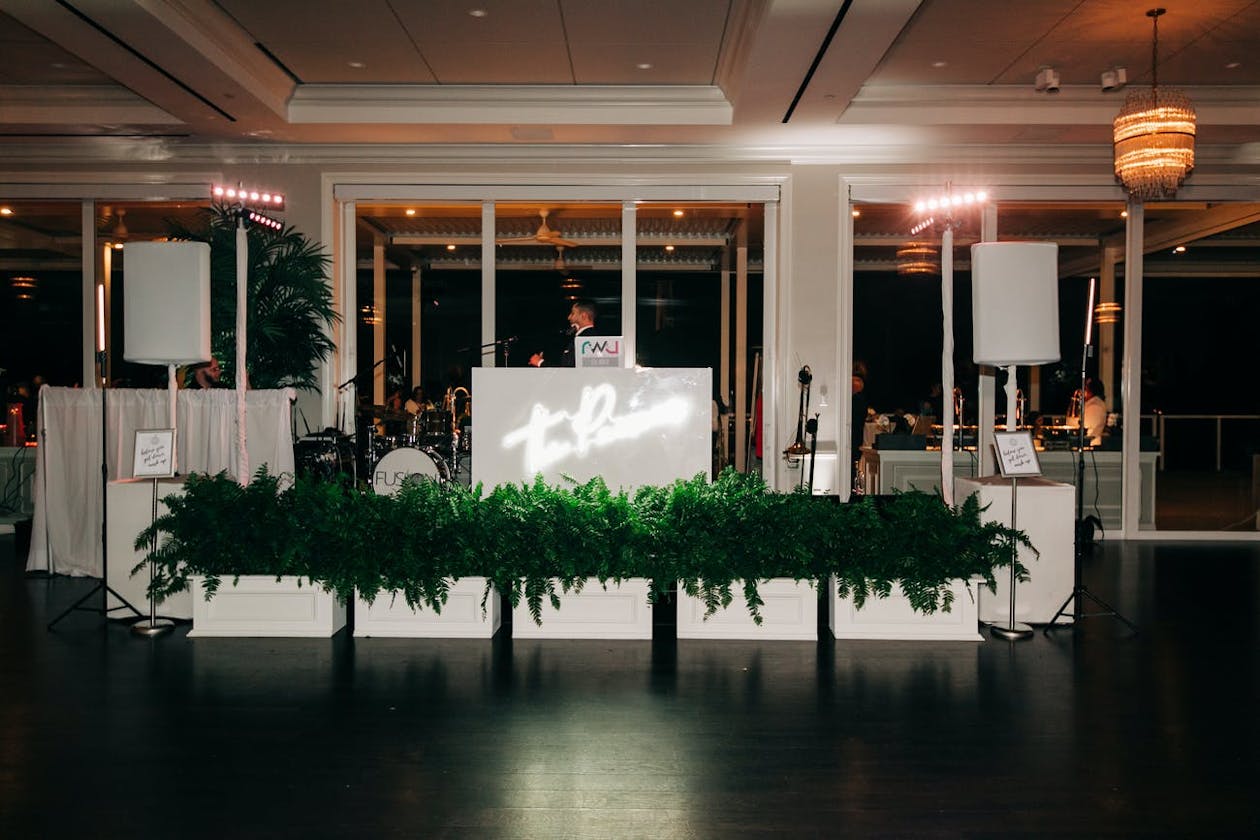 Greenery On DJ Booth and Stage with Custom Neon Sign at Wedding | PartySlate