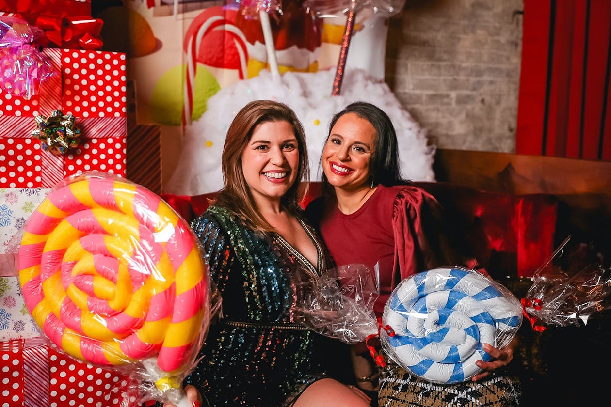 Two women hold giant lollipop props at Candy Land themed corporate event | PartySlate