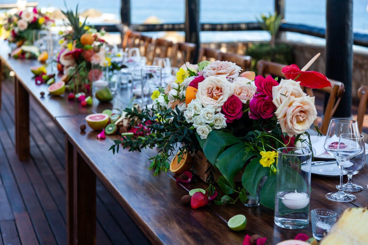 Wedding reception table lined with tropical colorful flowers and fruits | PartySlate