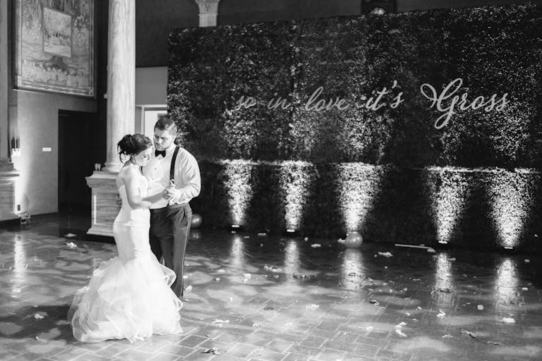 Black and White Photo of Couple Dancing On Dance Floor At Wedding In Front Of Greenery Wall With Custom Sign | PartySlate