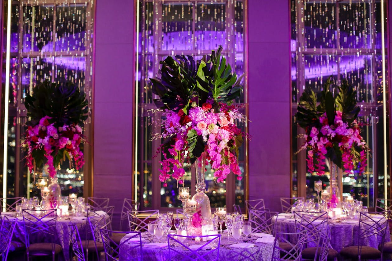 Tropcial ballroom wedding with purple uplighting and towering palm leaf centerpieces with pink orchid tendrils | PartySlate