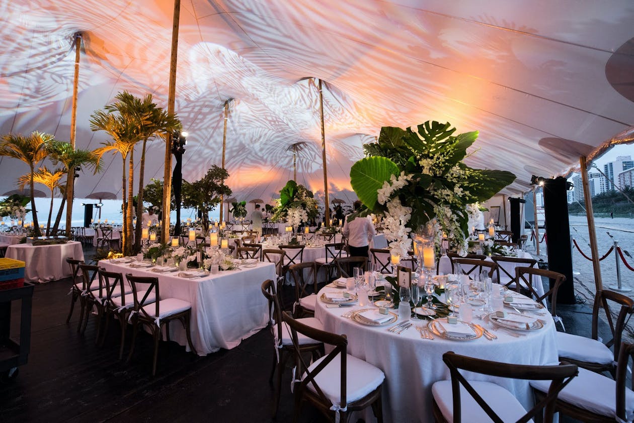 Tented wedding with lighting patterns on ceiling and large palm leaf centerpieces | PartySlate
