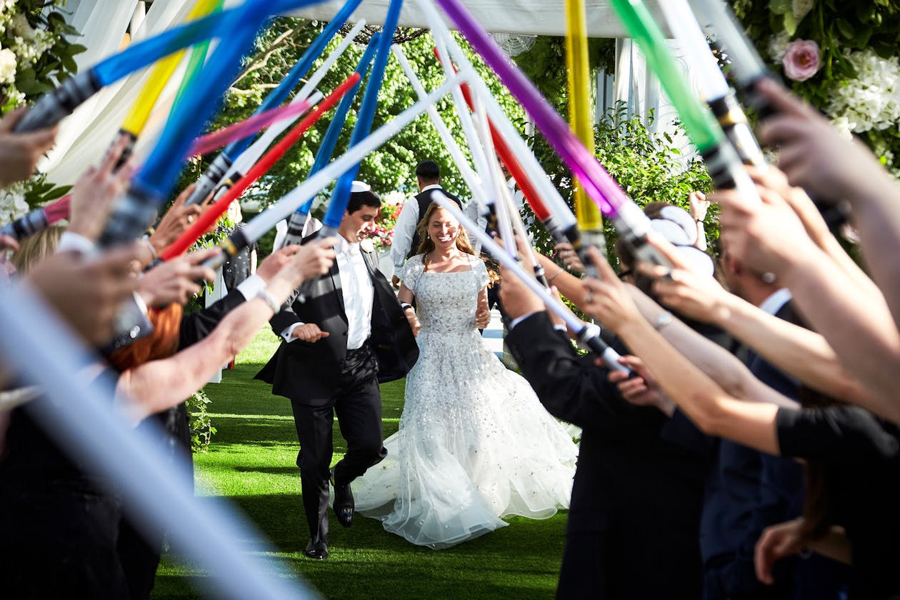 Tasteful and Alluring Wedding in Northbrook, Illinois Couple Leaving Wedding venue As Guests Wave Light Sabers | PartySlate