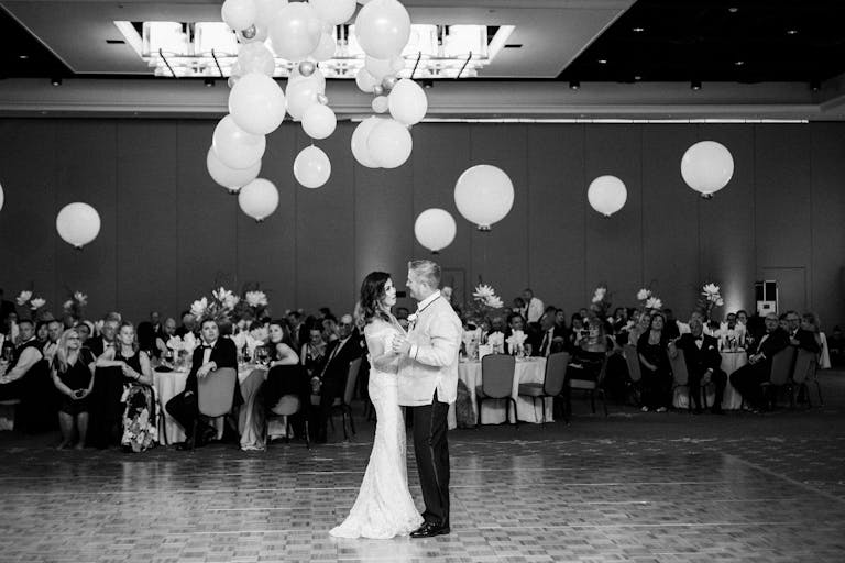 Black and White Photo of Couple Dancing on Wedding Dance Floor While White Balloons Fall From the Ceiling | PartySlate
