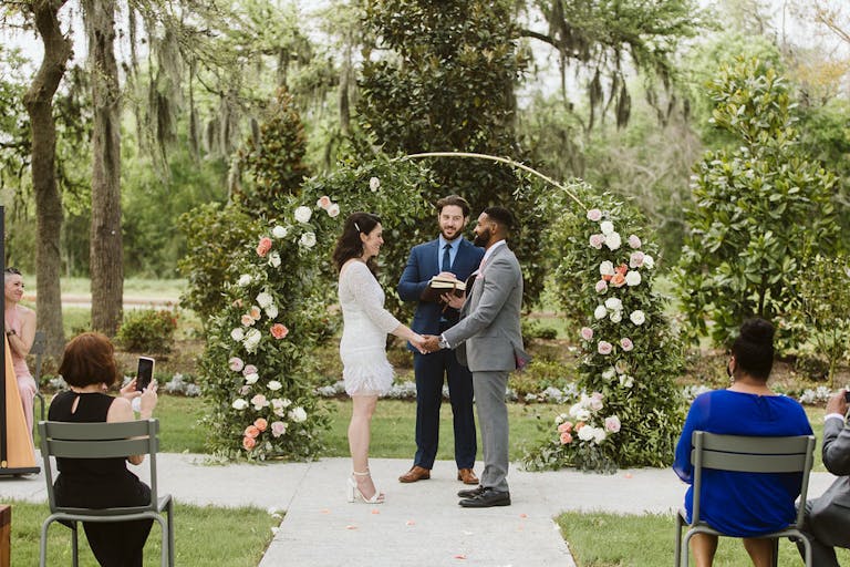 Stunning Outdoor Wedding WIth Couple Walking Down Aisle and Guests Seated and Colorful Floral Arch | PartySlate