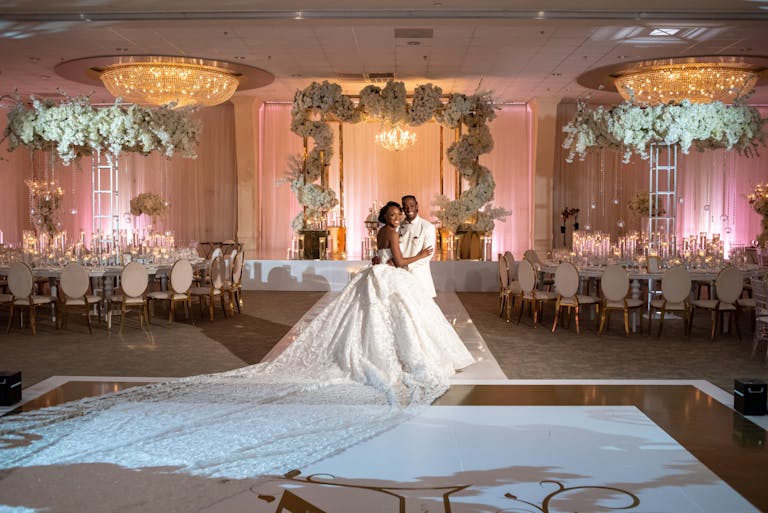 Stunning Indoor Wedding With Couple Posing In Front Of Tables and White Floral Décor | PartySlate