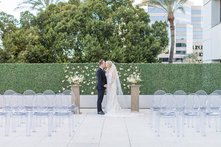 Couple Kissing At Outdoor Alter With Greenery and A Few White Flowers | PartySlate