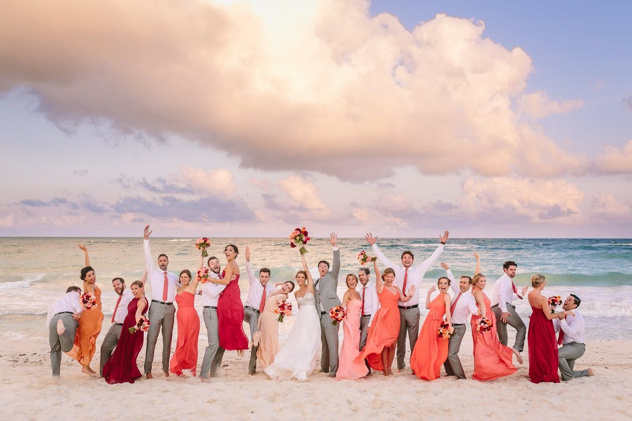 Wedding party in pink beach wedding colors jump for joy in surf | PartySlate