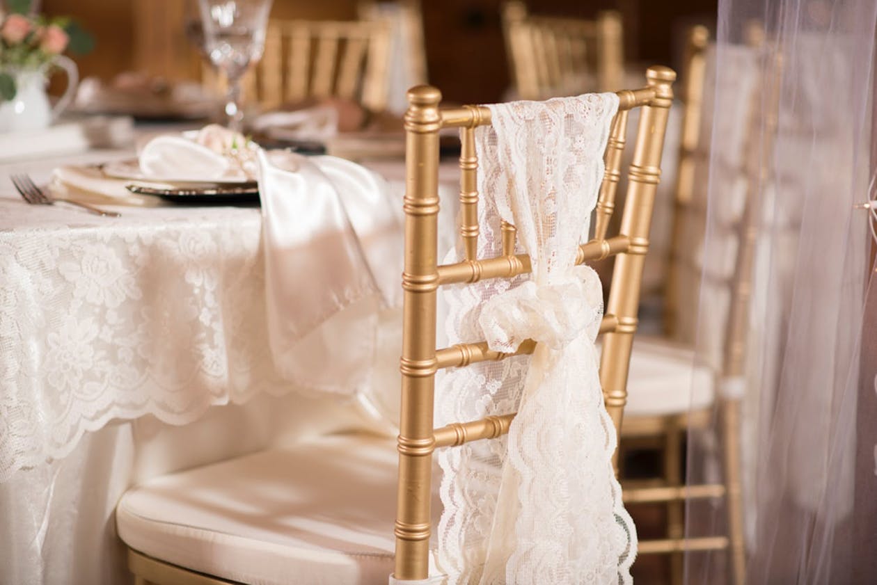 Vintage wedding theme with gold reception chairs draped in lace | PartySlate