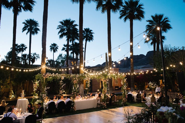 Outdoor wedding At Night With String Lights Hung Over Dance Floor and Tables With Guests Eating | PartySlate