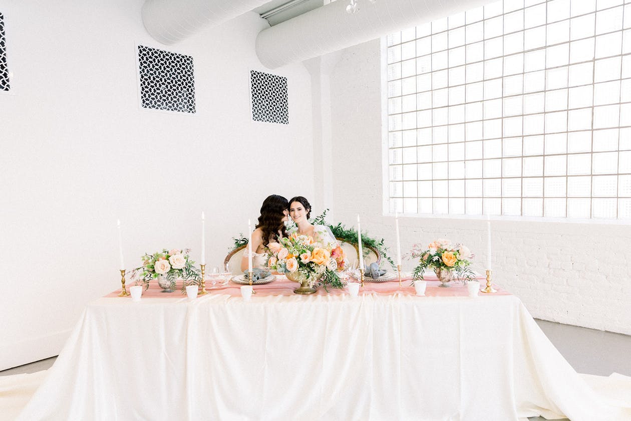 Brides at Head Table With Colorful Spring Wedding Centerpiece in White Venue | PartySlate