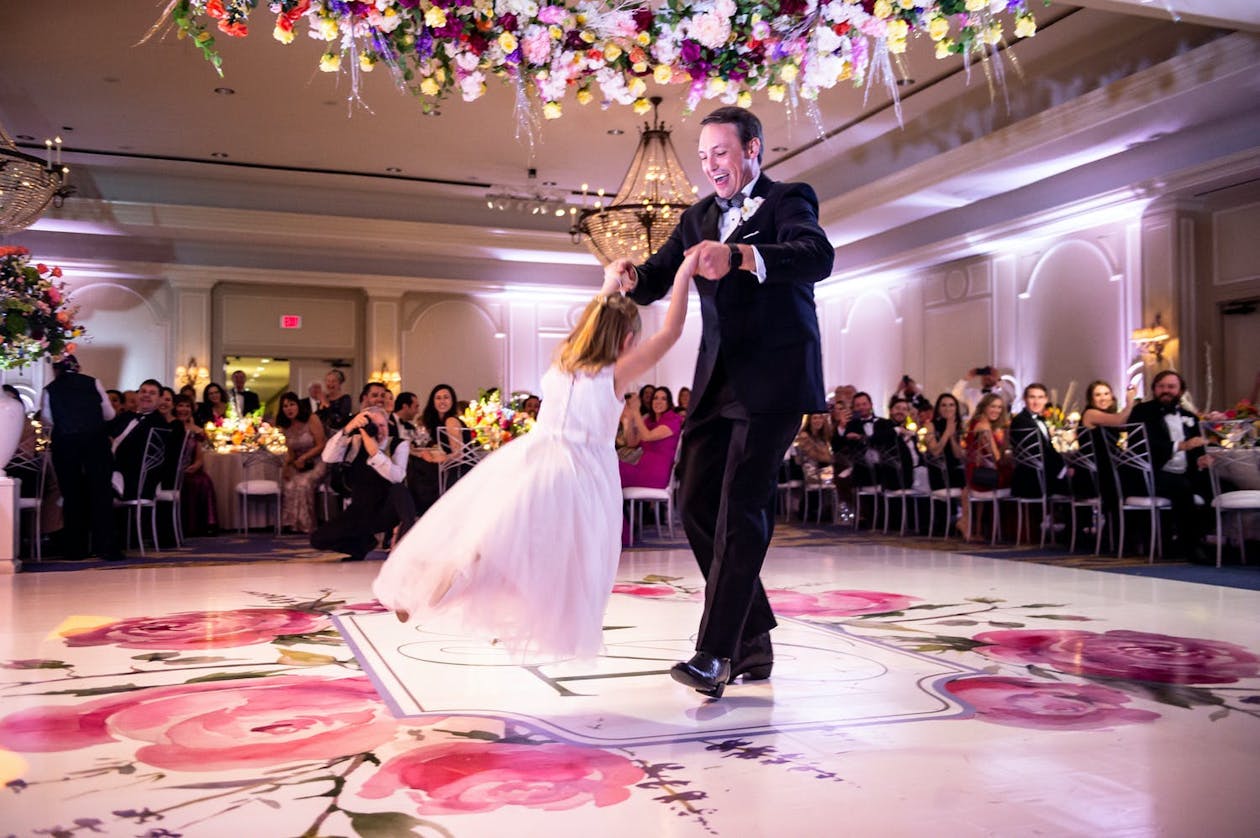 Man in tux dances with flower girl on pink flower dance floor | PartySlate