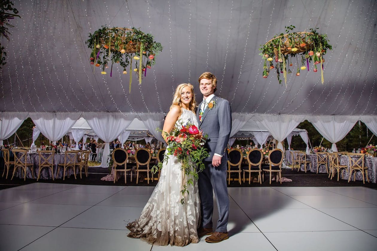 Bride and groom at tented wedding with suspended greenery | PartySlate