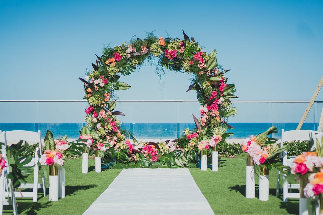 Circular arch with pink and orange flowers and greenery at beach wedding | PartySlate