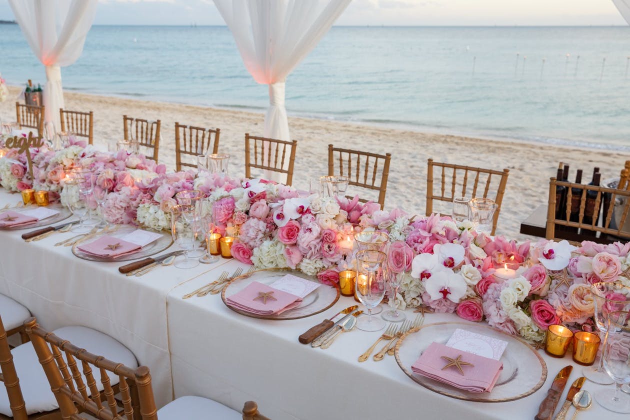 Wedding reception table on beach filled with flowers in pink and white beach wedding colors | PartySlate