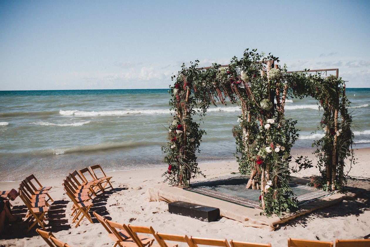 Beach wedding chuppah with wild greenery and burgundy and maroon flowers | PartySlate