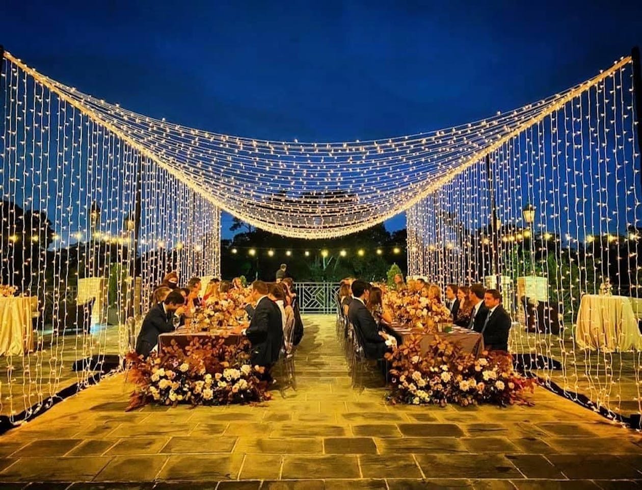 two tables with guests seated at both under string lights | PartySlate