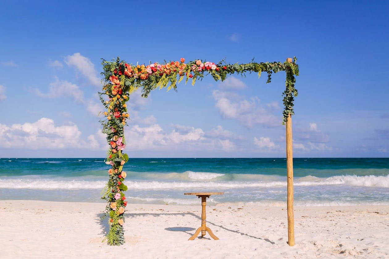 Square wedding arch with orange and pink flowers at beach tropical wedding | PartySlate
