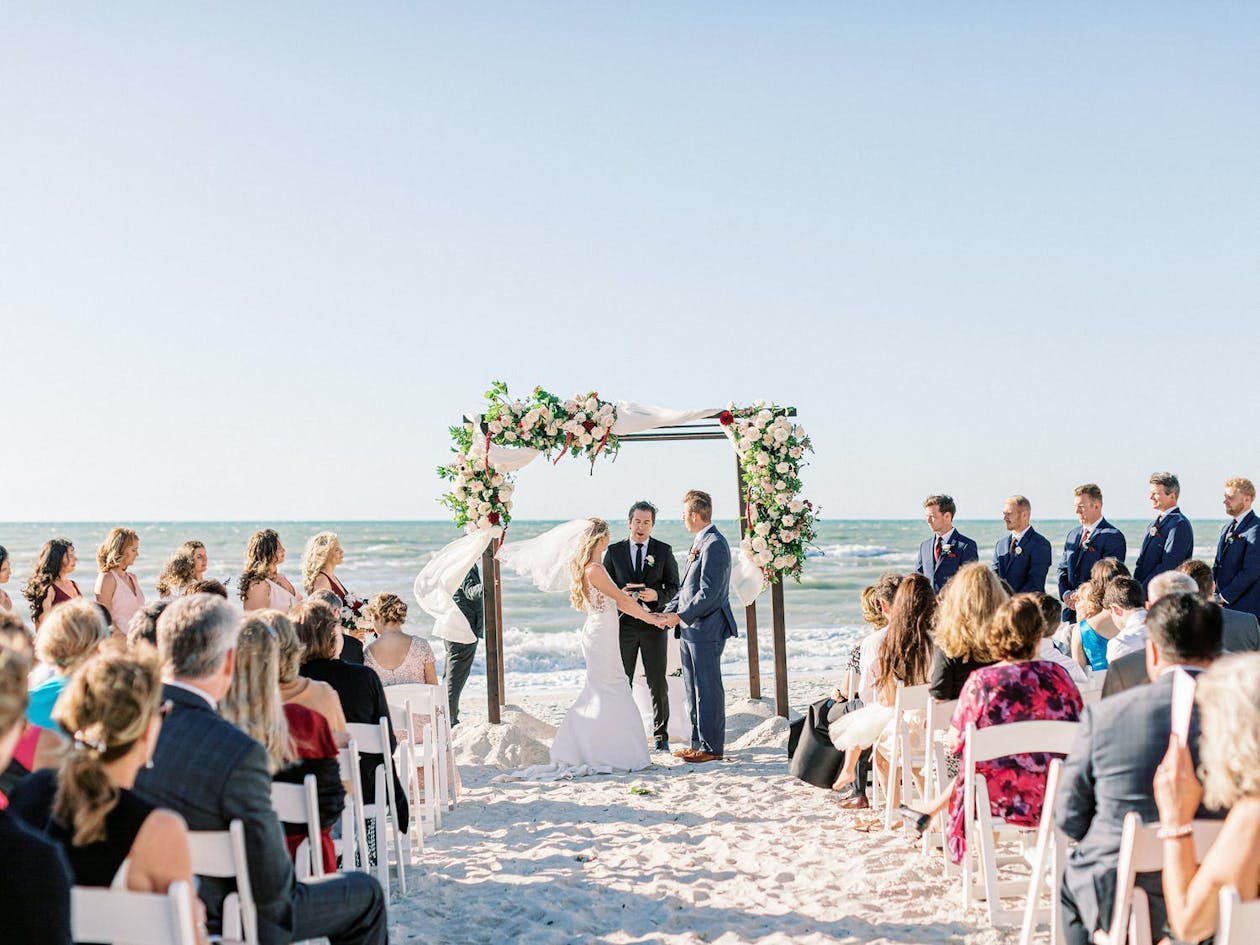 Romantic ocean-front wedding ceremony in peach and burgundy and maroon | PartySlate