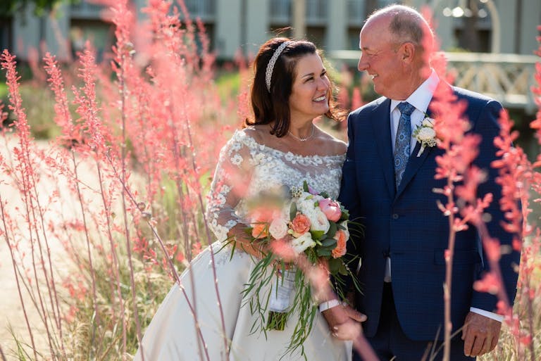 Couple Getting married Outdoors Smiling While Walking Through Pink Brush Flowers | PartySlate