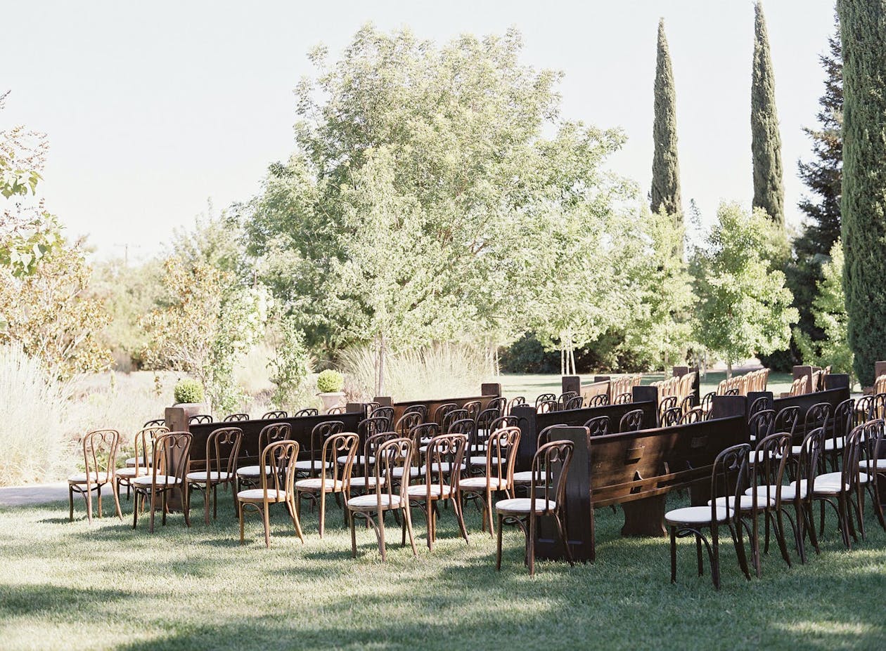 Outdoor vintage wedding theme with pew seating and bentwood cafe chairs | PartySlate