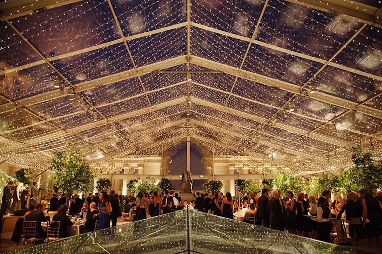 Classic Tented Wedding At Night With Twinkle Lights And Guests eating Dinner | PartySlate