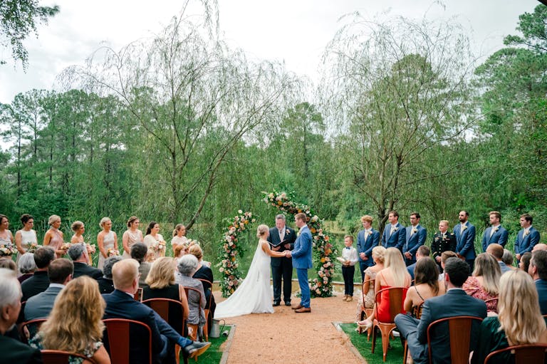 Stunning Outdoor Wedding WIth Couple Walking Down Aisle and Guests Seated and Colorful Floral Arch | PartySlate