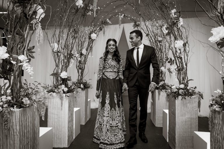 Black and White Photo of Traditional Indian Wedding With Couple Standing Under Floral Arches Inside | PartySlate