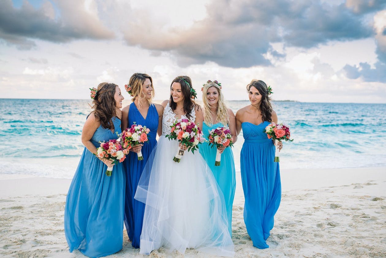 Bride with bridesmaids in blue dresses walk the beach | PartySlate