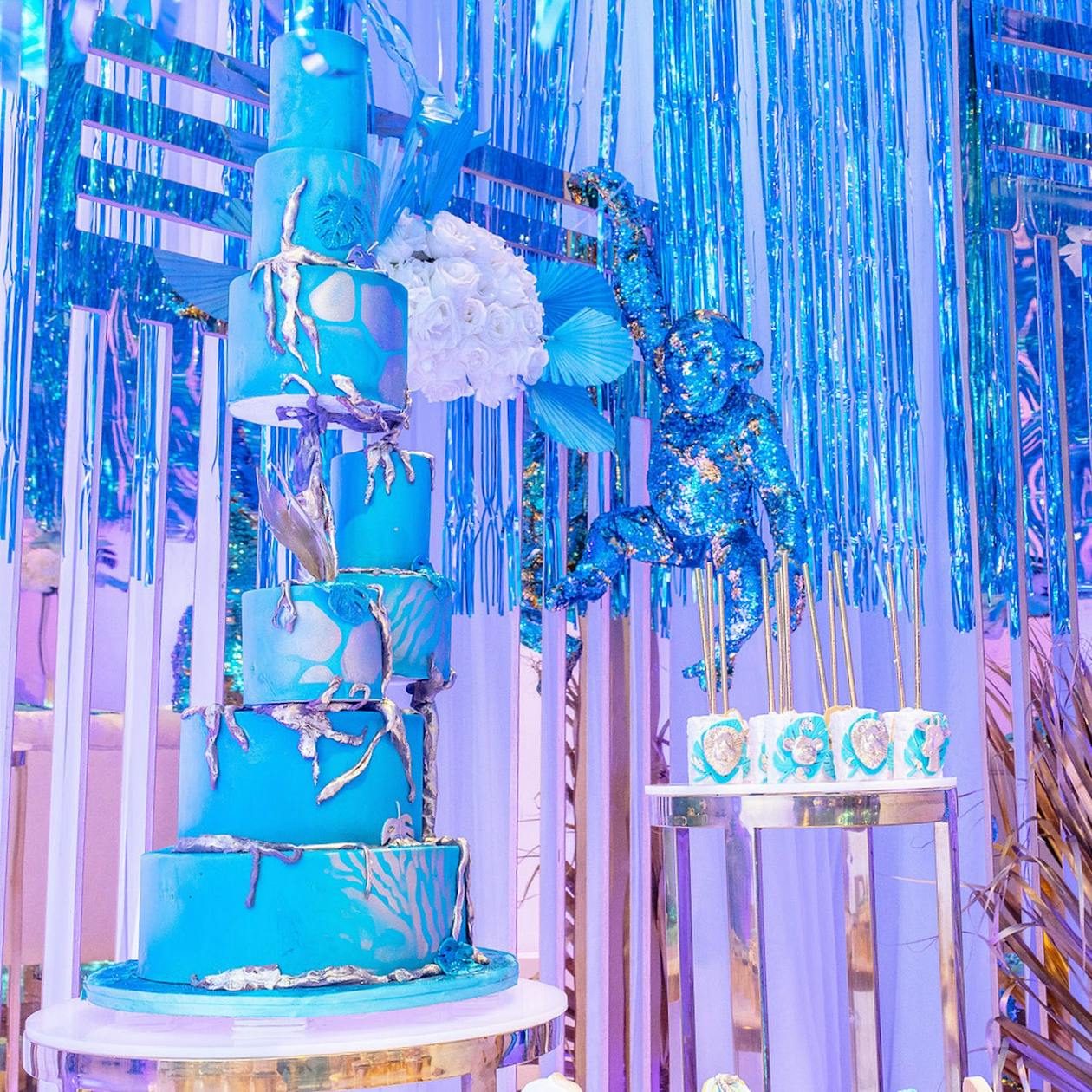 Towering blue cake with silver icing against iridescent blue fringe backdrop | PartySlate