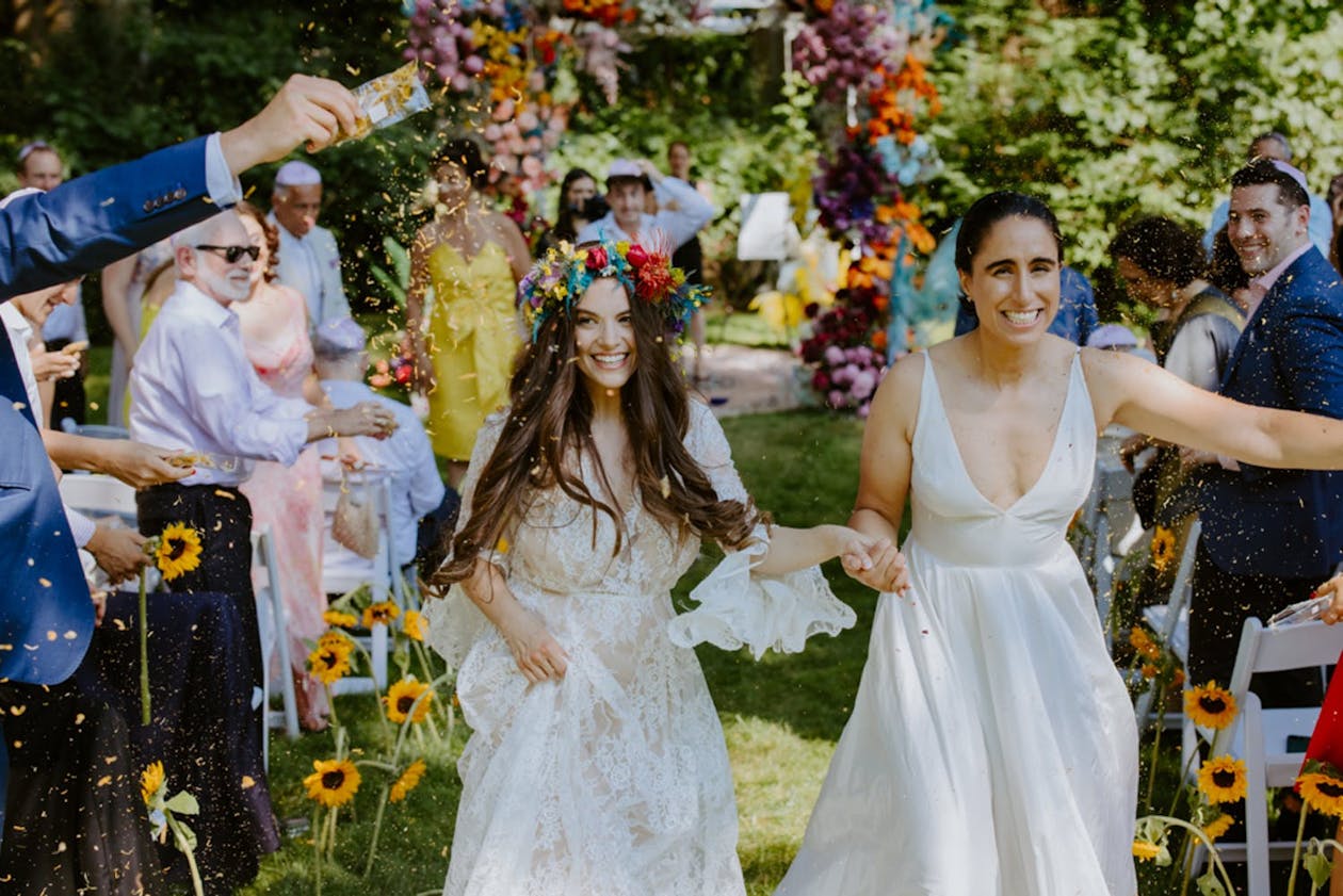 Two brides exit wedding aisle at colorful and whimsical wedding | PartySlate