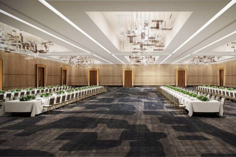 Hotel ballroom reception area with long dining tables with white linen and greenery centerpieces | PartySlate
