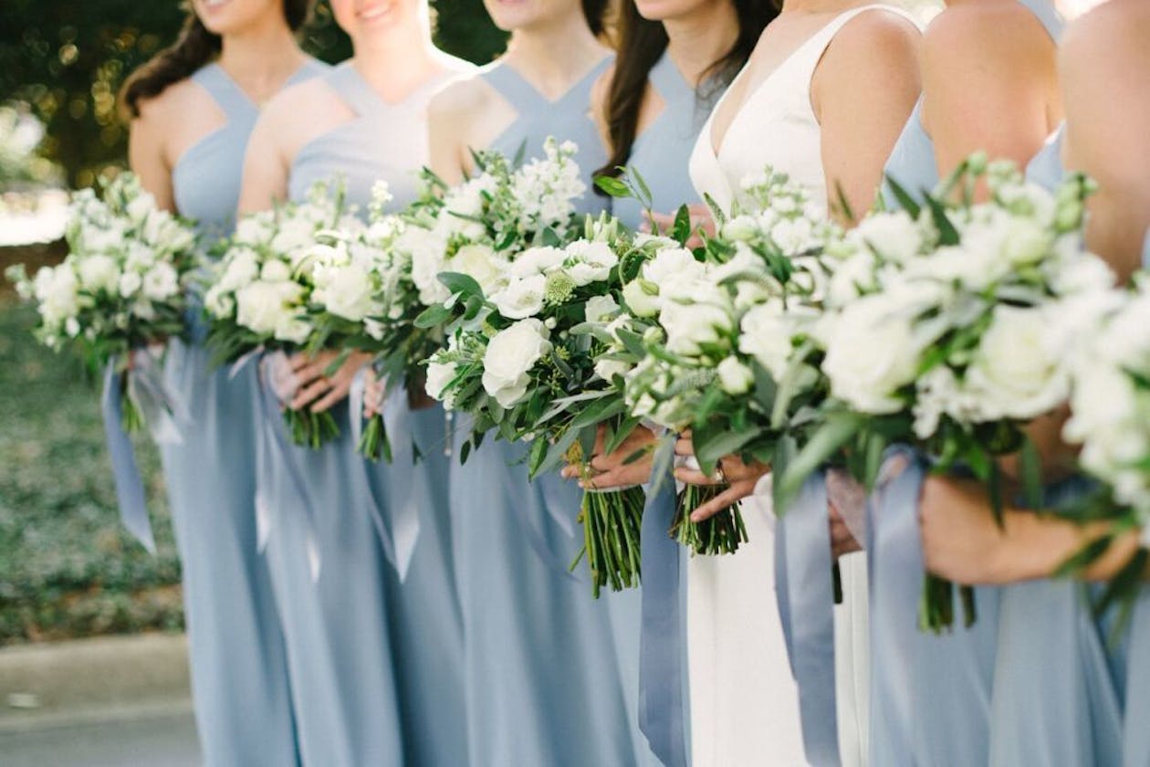 Bridal party in powder blue dresses hold white floral bouquets | PartySlate