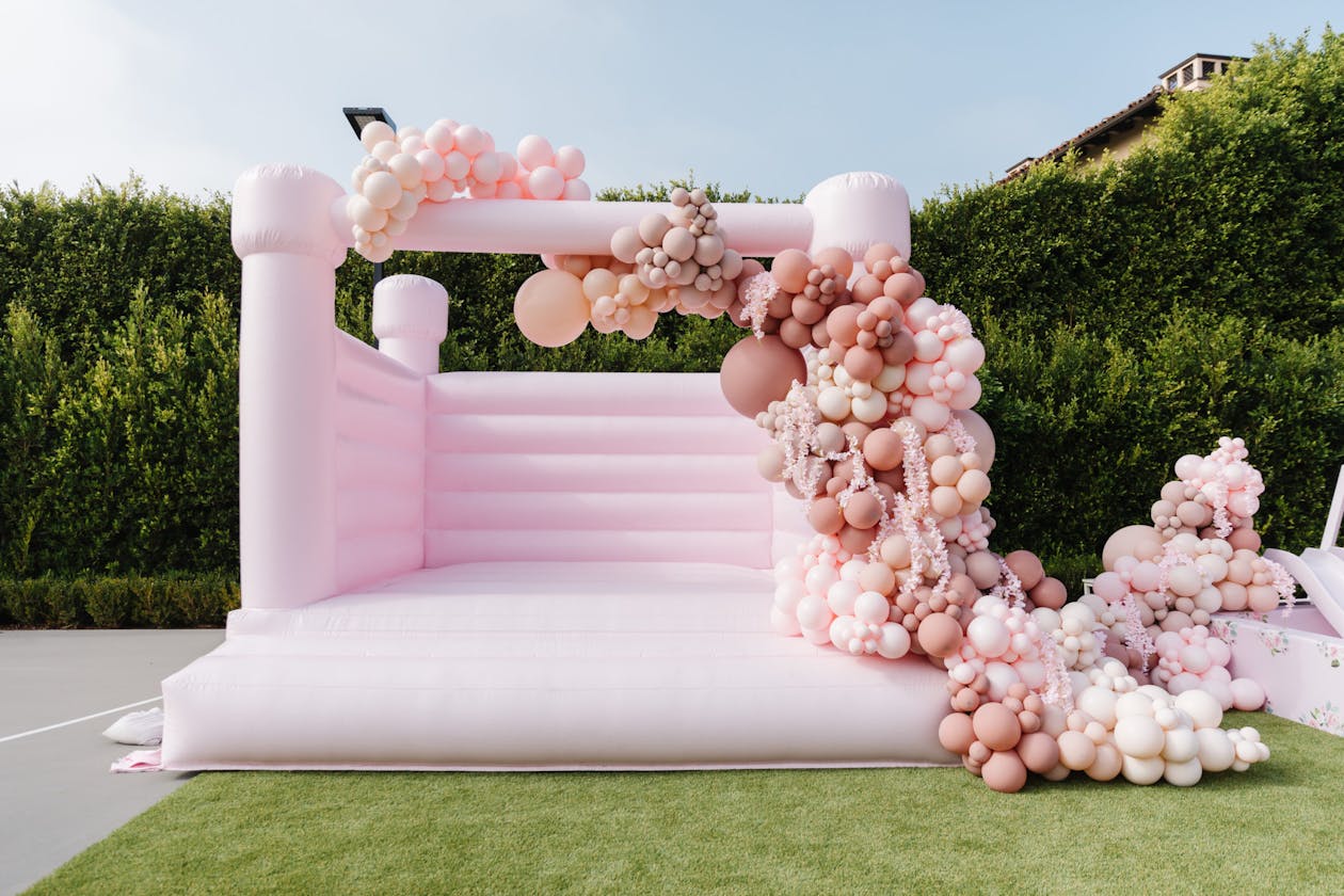 pastel pink bounce house at kids birthday party covered in pink balloons | PartySlate
