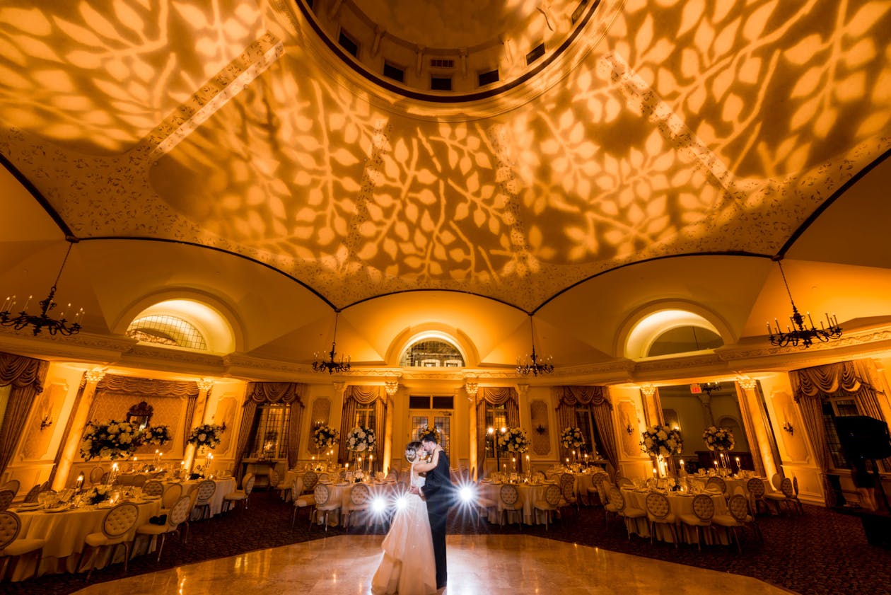 Bride and groom first dance in ballroom with amber leaf projection lighting | PartySlate