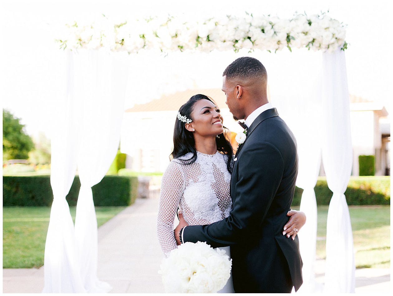 Timeless black and white wedding with white floral wedding arch with drapery outside | PartySlate