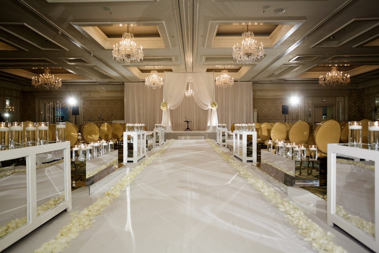 Indoor All White wedding aisle with flowers on either side and floral arch at alter| PartySlate