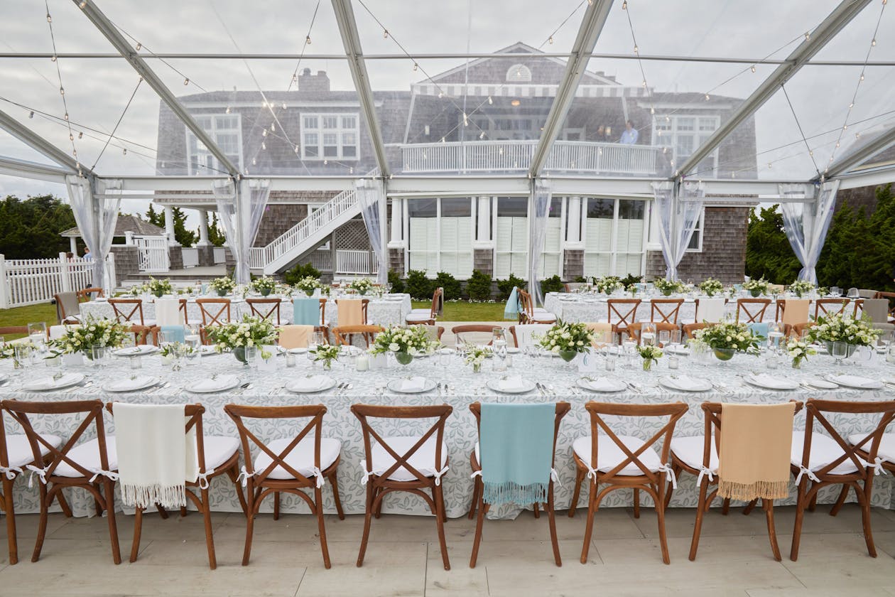 Transparent tented wedding in Hamptons with light blue and apricot-colored shawls intermittently draped over seating | PartySlate