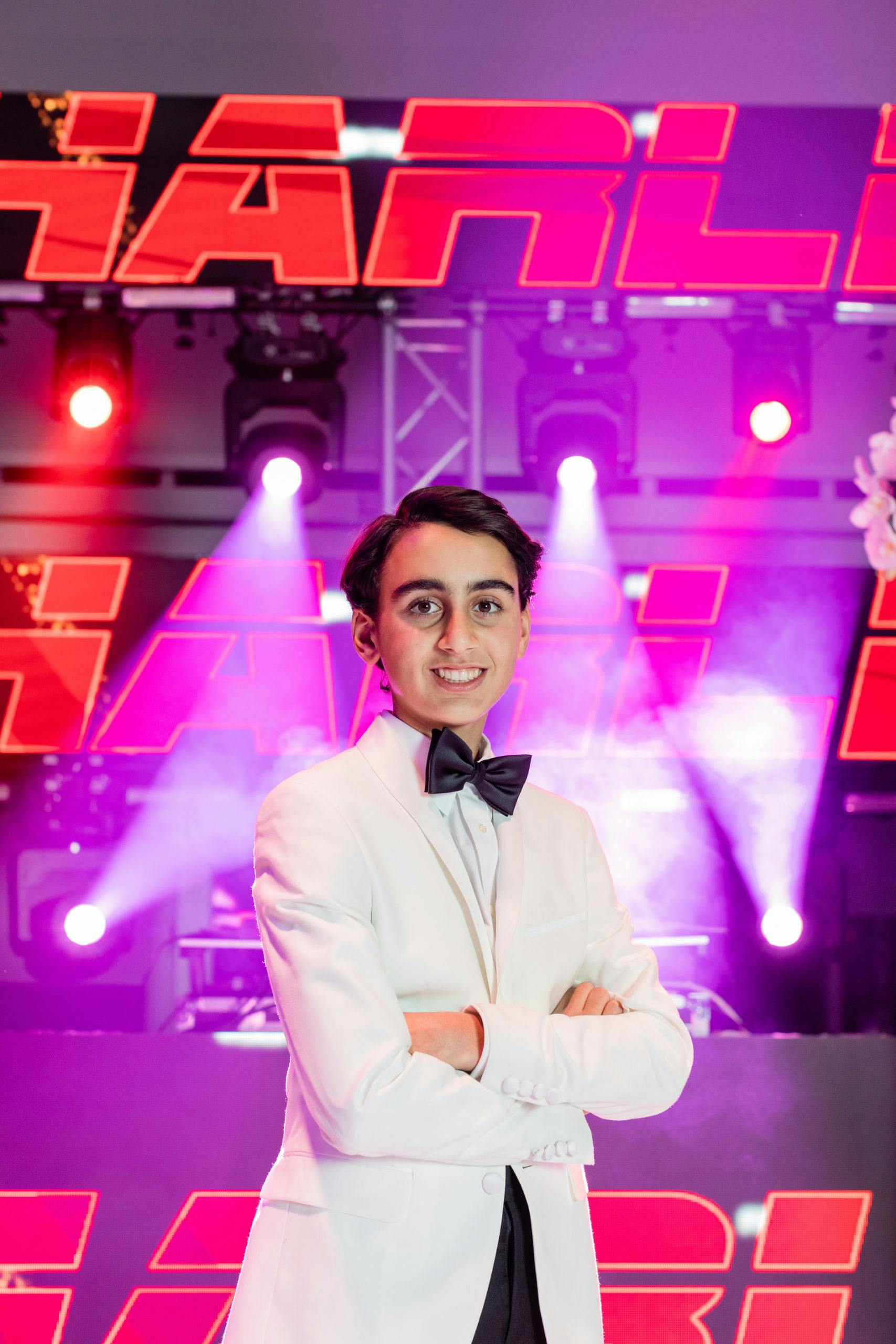 Bar Mitzvah boy stand in front of pink and purple lighting display | PartySlate