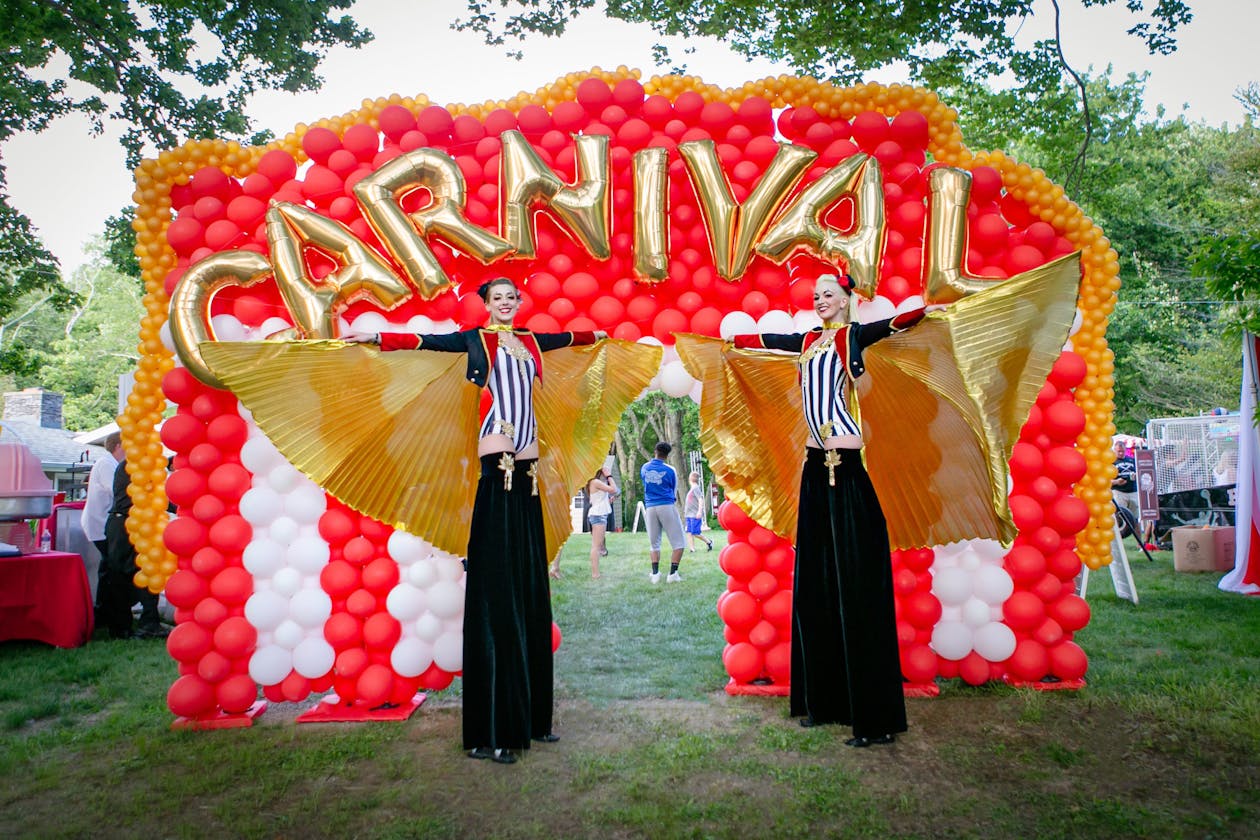 Carnival themed graduation party with red and yellow balloon arch entrance and performers on stilts | PartySlate