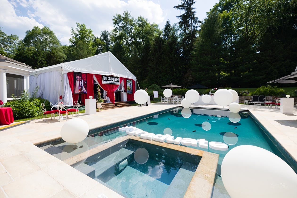 backyard Graduation party with tent and floating graduate letters in the pool with balloons | PartySlate