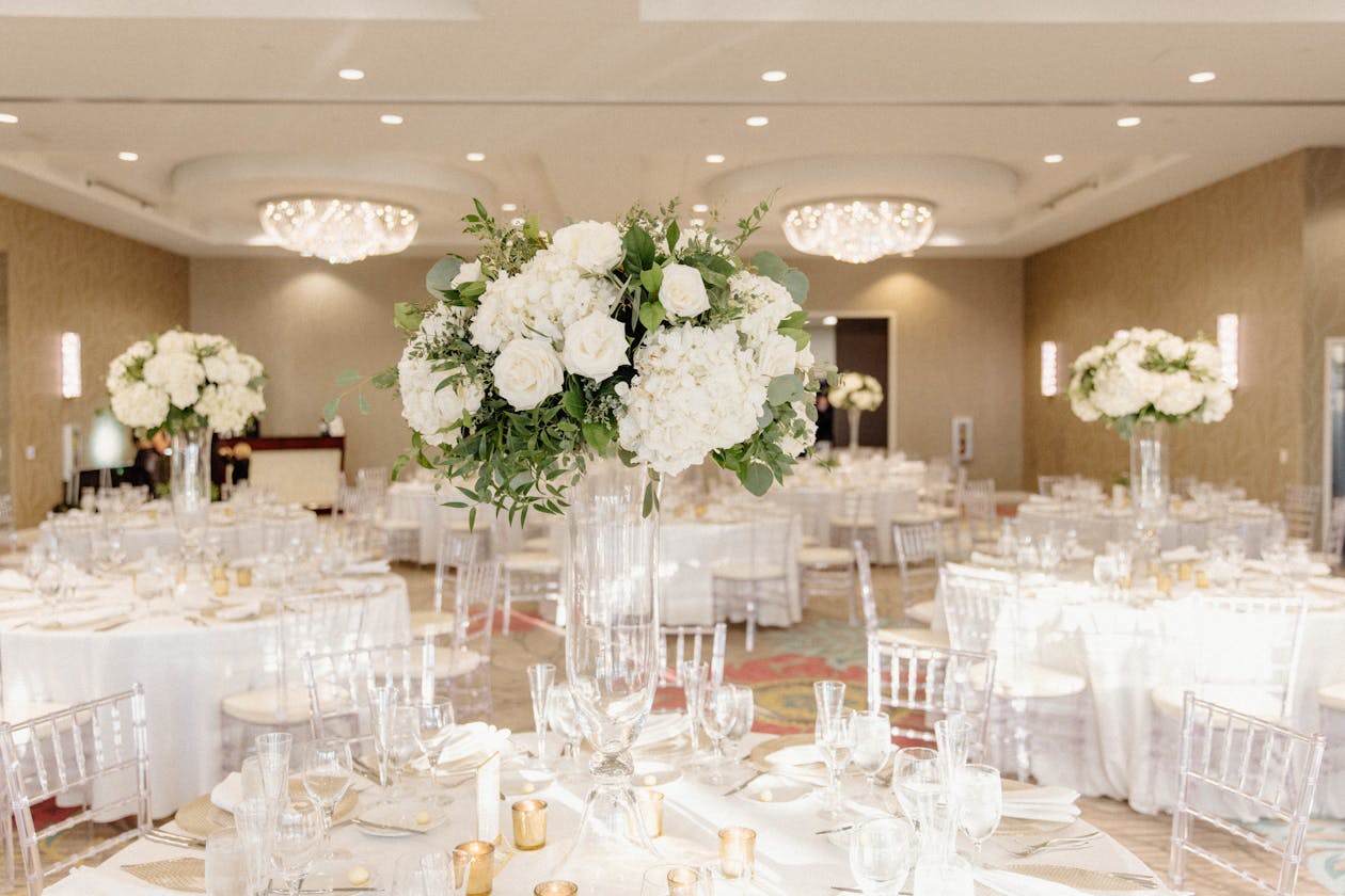 White and green tall centerpieces on round tables in reception hall | PartySlate