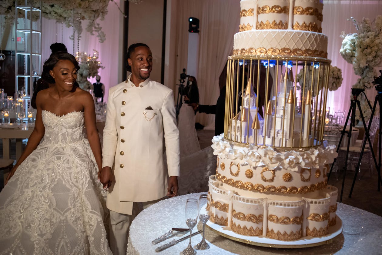 Couple stand near towering wedding cake with intermittent castle tier | PartySlate