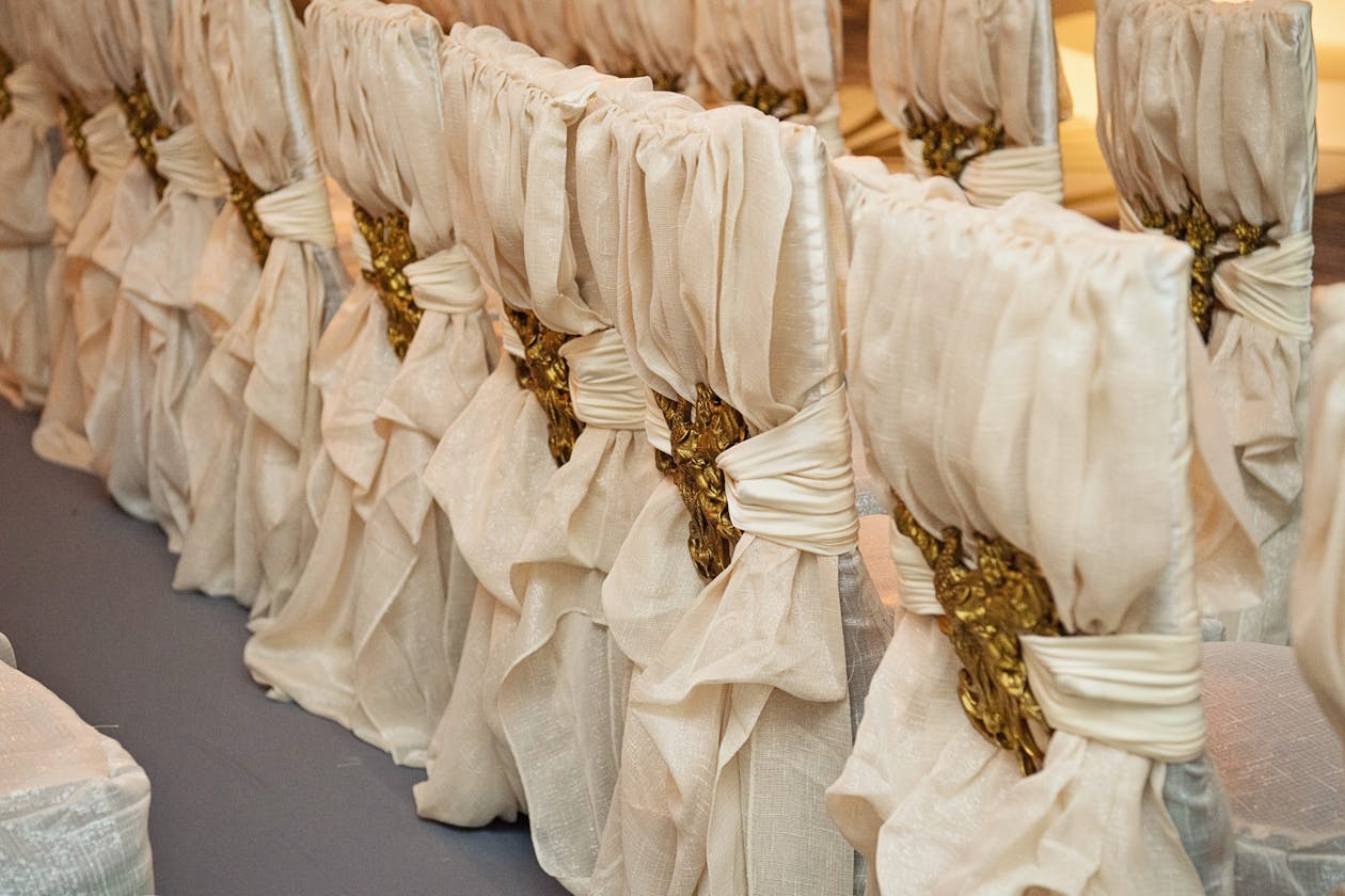 Wedding ceremony chairs wrapped in luxe white drapery with gold backing | PartySlate